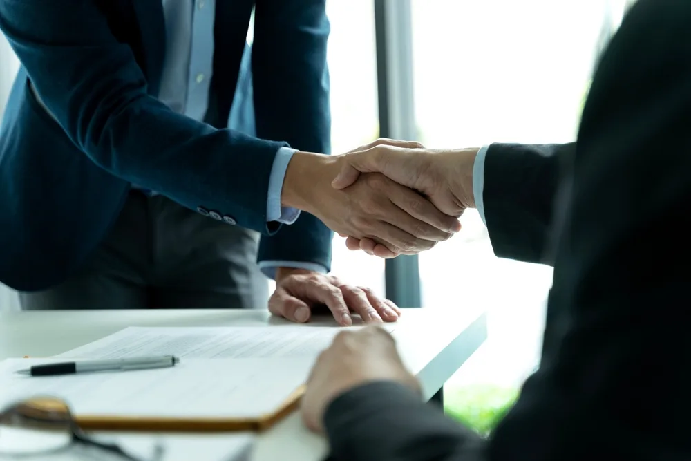 Two people shaking hands over documents on a table.